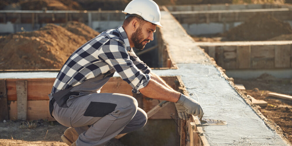 Sitting, working with foundation of the house. Man is on the construction site at daytime