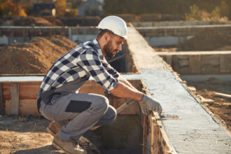 Sitting, working with foundation of the house. Man is on the construction site at daytime