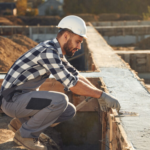 Sitting, working with foundation of the house. Man is on the construction site at daytime