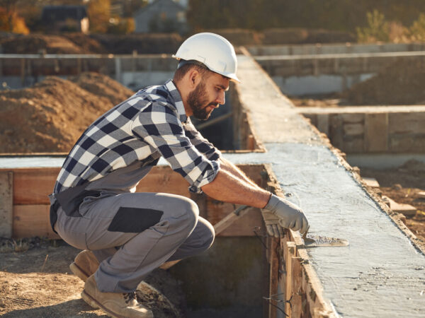 Sitting, working with foundation of the house. Man is on the construction site at daytime