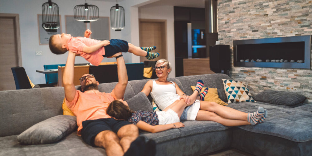 Family relaxing on the sofa while dad holds a young boy laughing up in the air