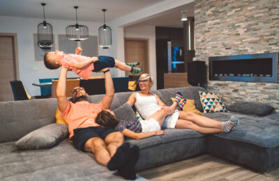 Family relaxing on the sofa while dad holds a young boy laughing up in the air