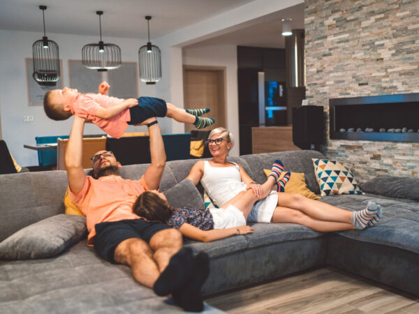 Family relaxing on the sofa while dad holds a young boy laughing up in the air